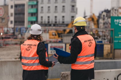 Deux personnes portant des casques de sécurité et des gilets fluorescents discutent sur un chantier.